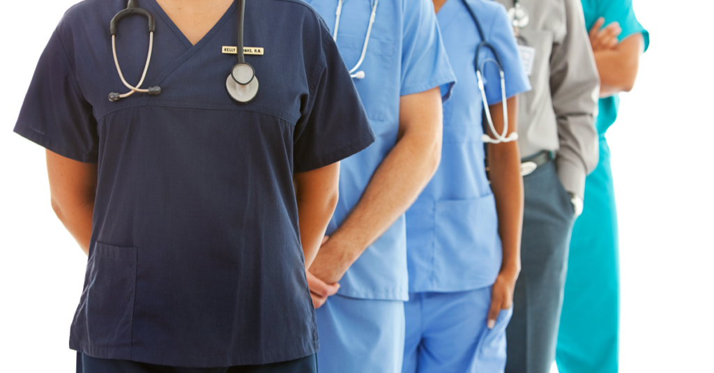 Five people standing in a row all facing forward wearing various healthcare worker uniforms.